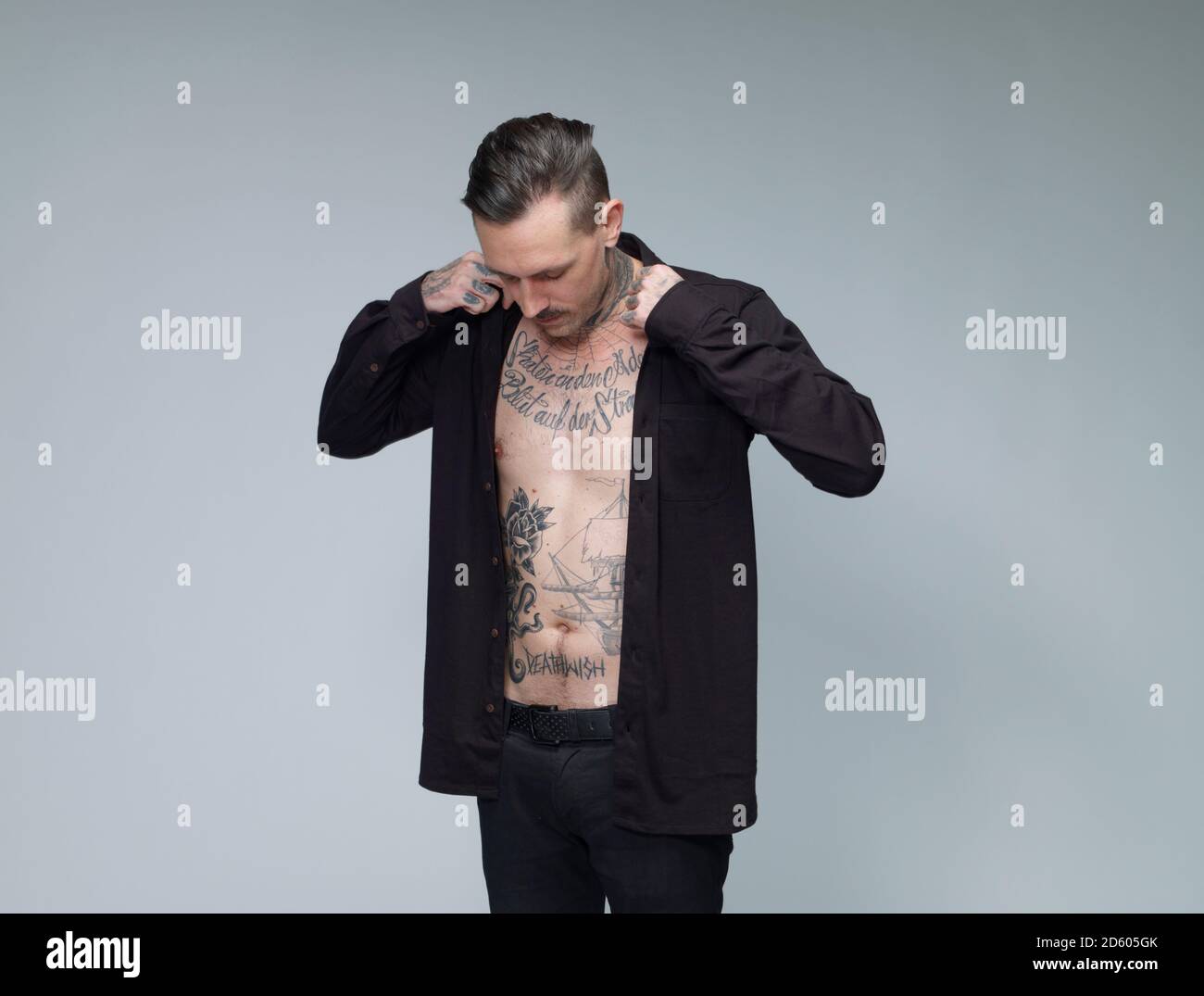Uomo con tatuaggio sulla sua vita fino medicazione camicia nera davanti a uno sfondo grigio Foto Stock