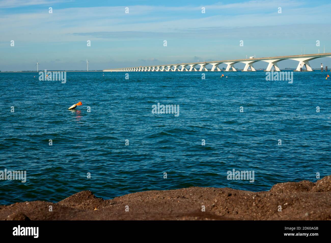 Long Zeeland Bridge, acque blu profonde con boa, alcune turbine eoliche sullo sfondo. Foto Stock