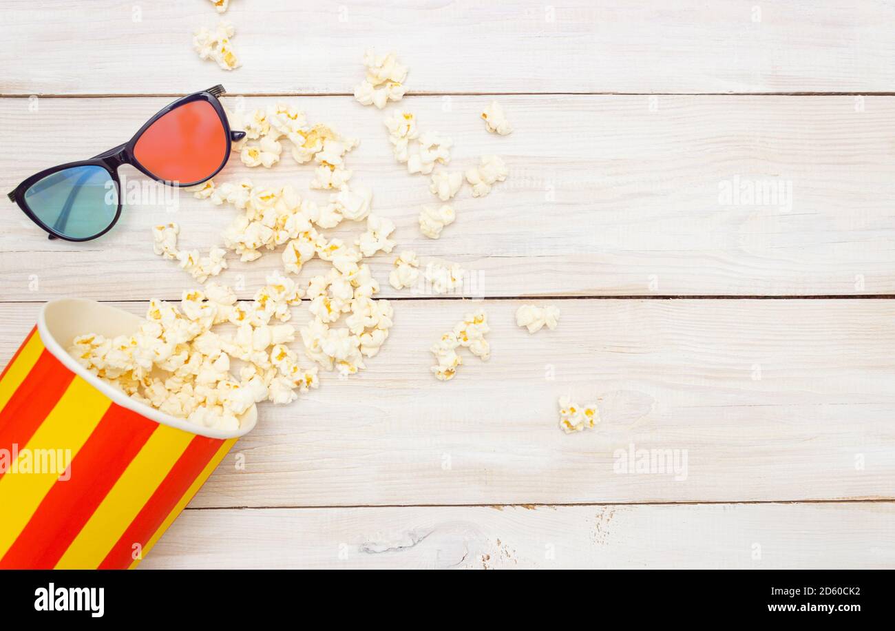 Anteprima concept del film. Il popcorn fuoriesce dalla scatola e dagli occhiali 3D. Sfondo in legno chiaro, spazio libero per il testo, vista dall'alto. Foto Stock