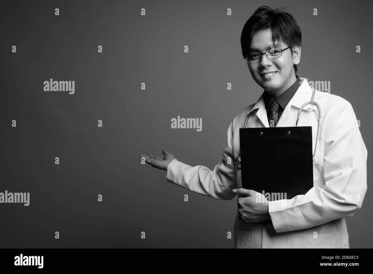 Giovane bel medico asiatico uomo che indossa occhiali su sfondo grigio Foto Stock