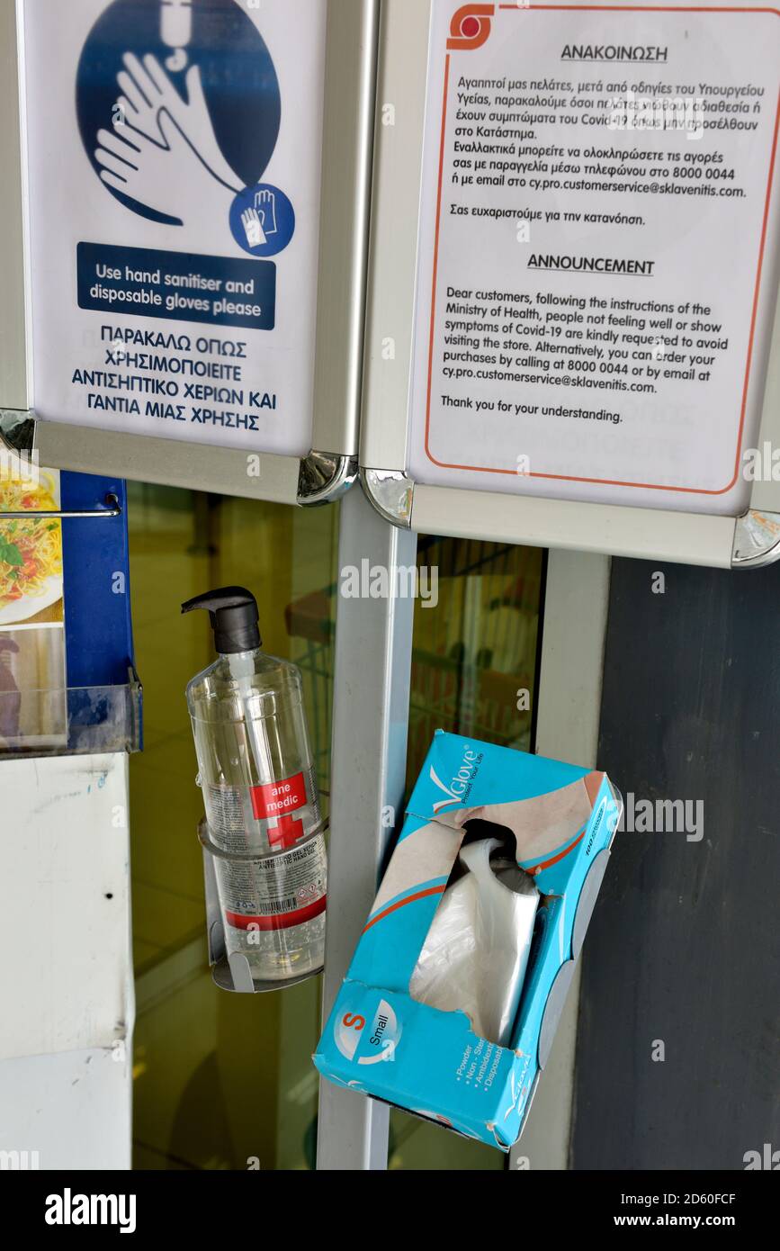 Igienizzatore per le mani in dispenser con scatola di guanti di plastica monouso e firmare dicendo di usarli Foto Stock