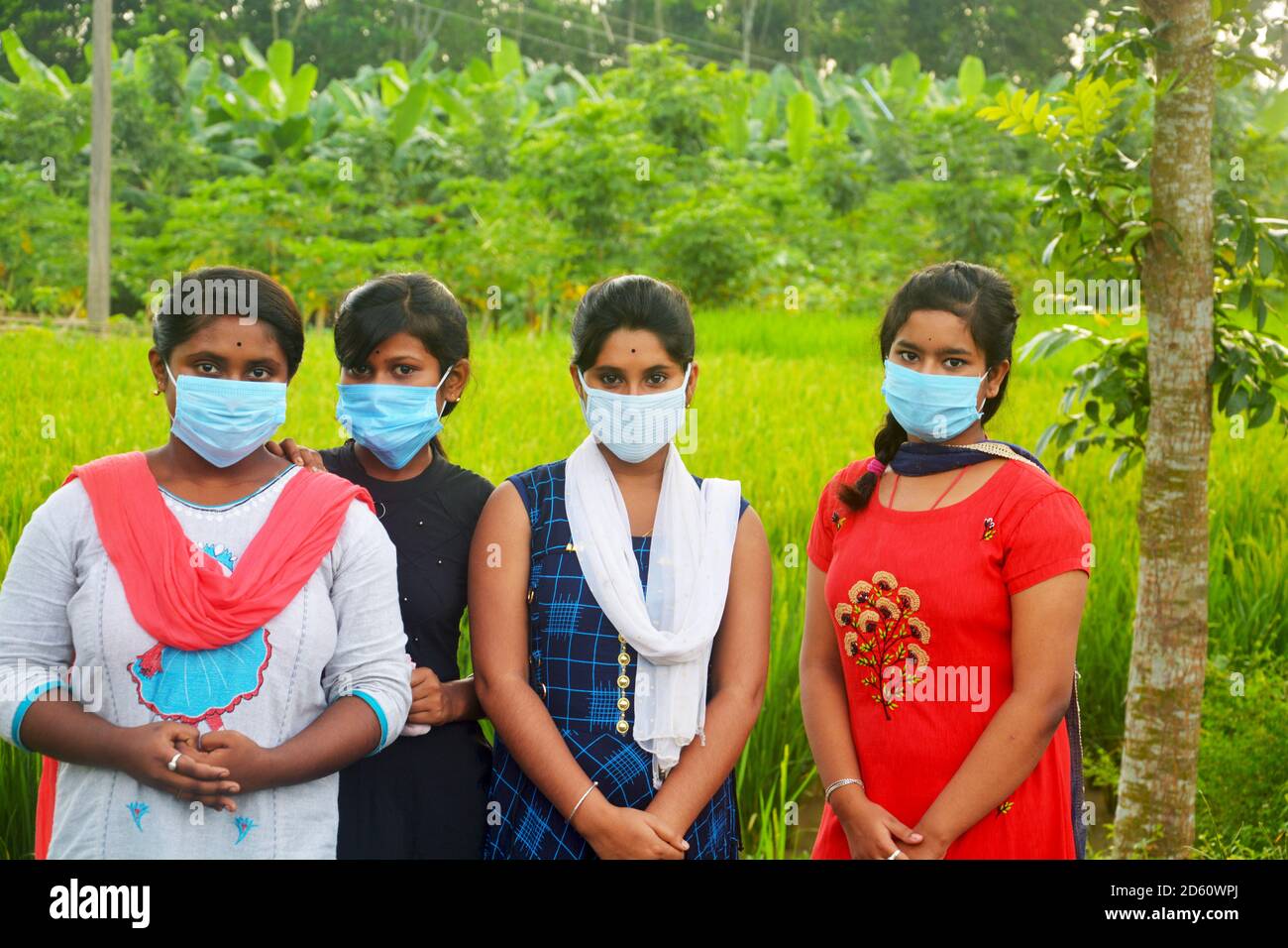 Primo piano di quattro ragazze adolescenti che indossano la maschera facciale in piedi in un campo di risaie agricolo, messa a fuoco selettiva Foto Stock