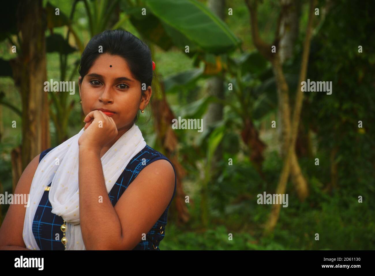Primo piano di una ragazza teenage indiana bengalese che indossa salwar blu e dhuppata bianca, in piedi con la mano sinistra sulla sua bocca, messa a fuoco selettiva Foto Stock