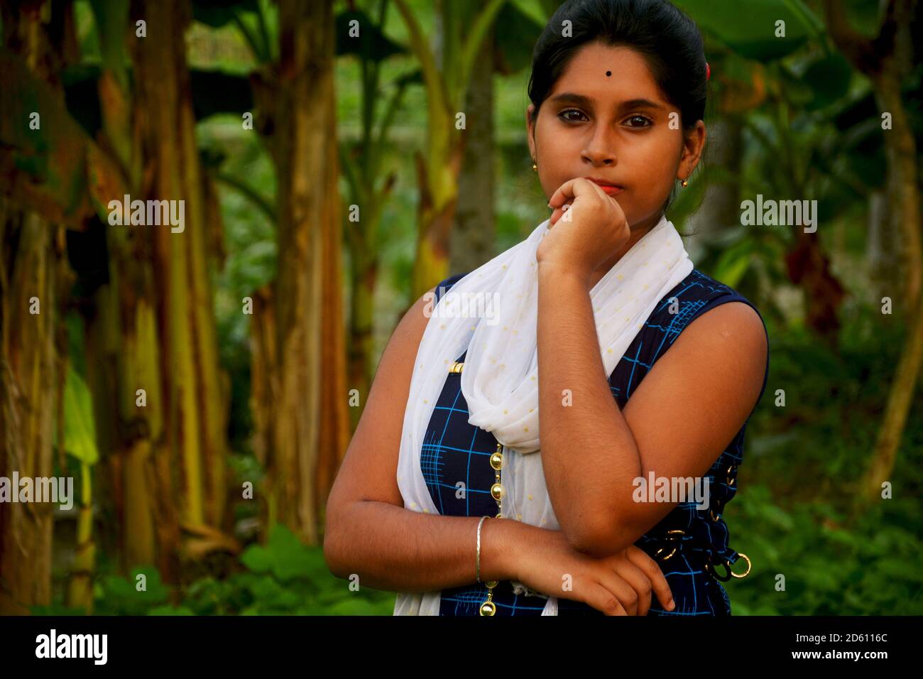 Primo piano di una ragazza teenage indiana bengalese che indossa salwar blu e dhuppata bianca, in piedi con la mano sinistra sulla sua bocca, messa a fuoco selettiva Foto Stock