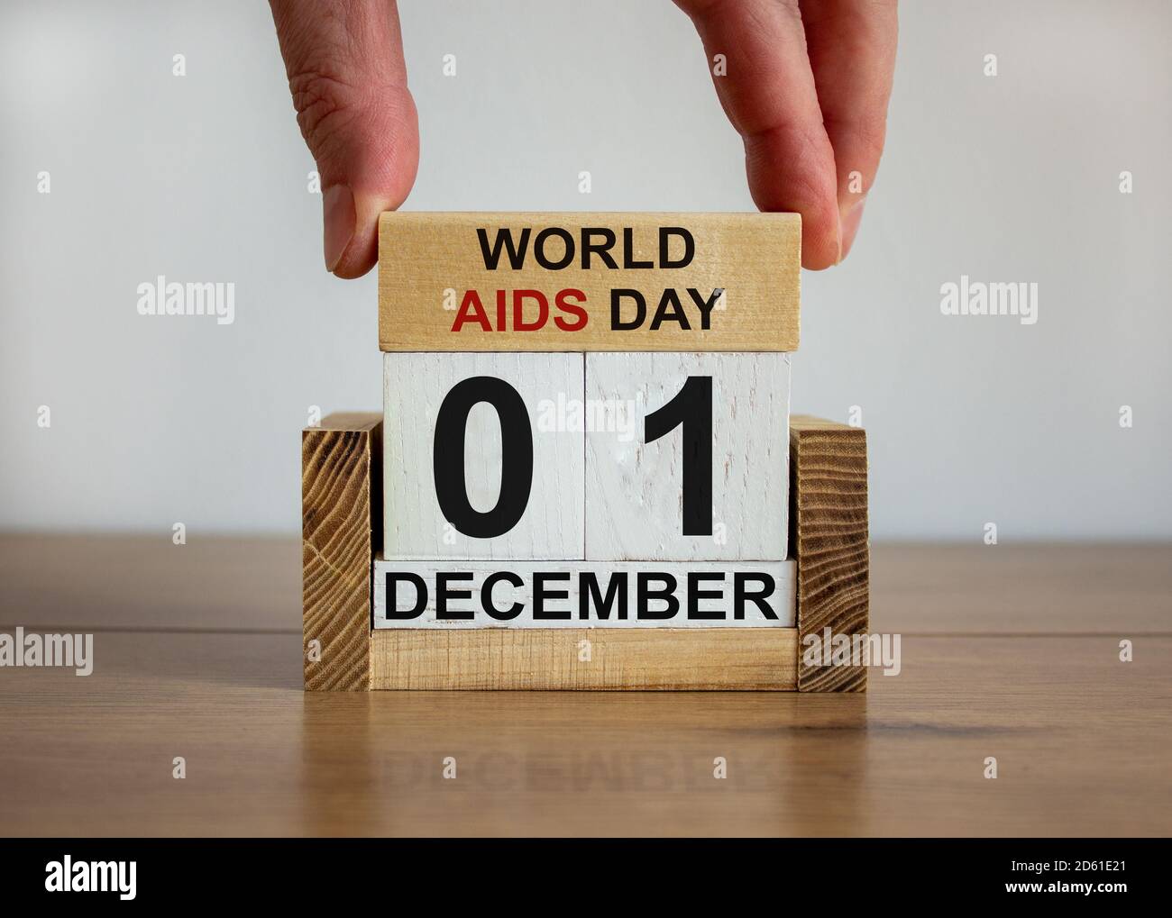 La mano maschile mette un blocco con l'iscrizione 'Giornata Mondiale dell'AIDS' su cubi con la data del 01 dicembre. Tavolo di legno. Splendido sfondo bianco, spazio per la copia. Foto Stock