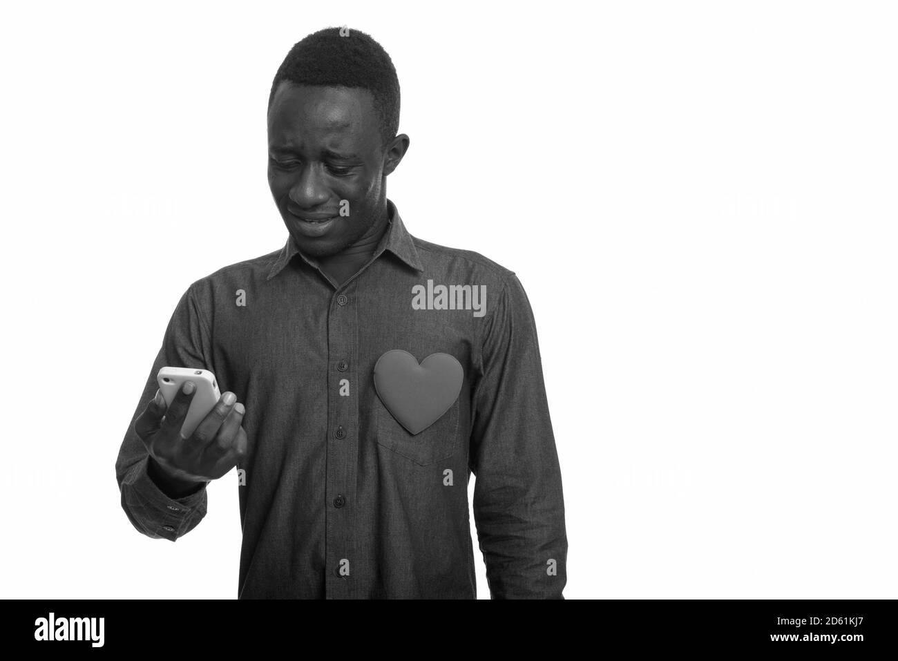Uomo africano triste usando il telefono cellulare con il cuore sul petto Foto Stock