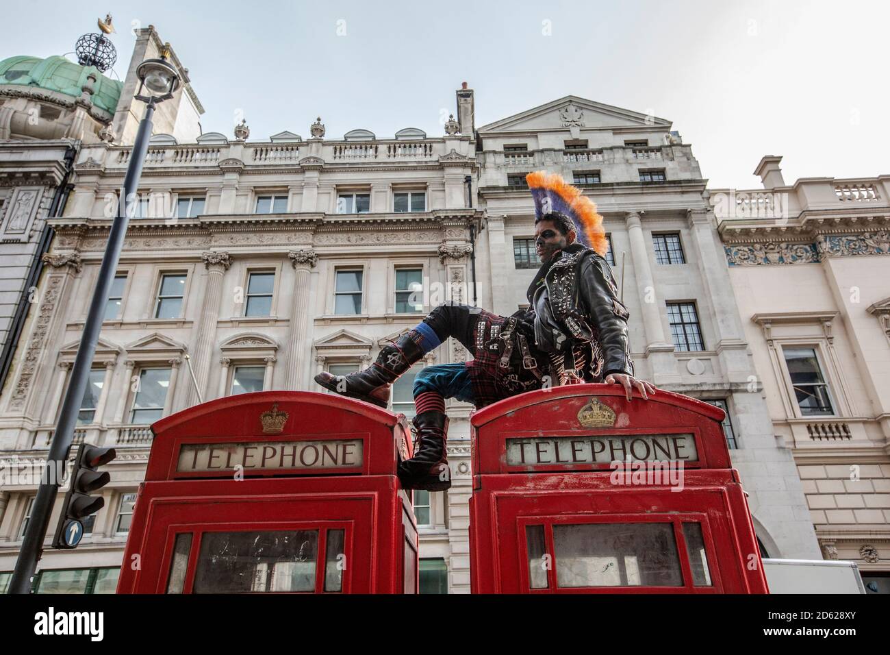 Punk rocker con capelli mohican si siede rilassante sulla parte superiore delle scatole rosse del telefono nel centro di Londra, Inghilterra, Regno Unito Foto Stock