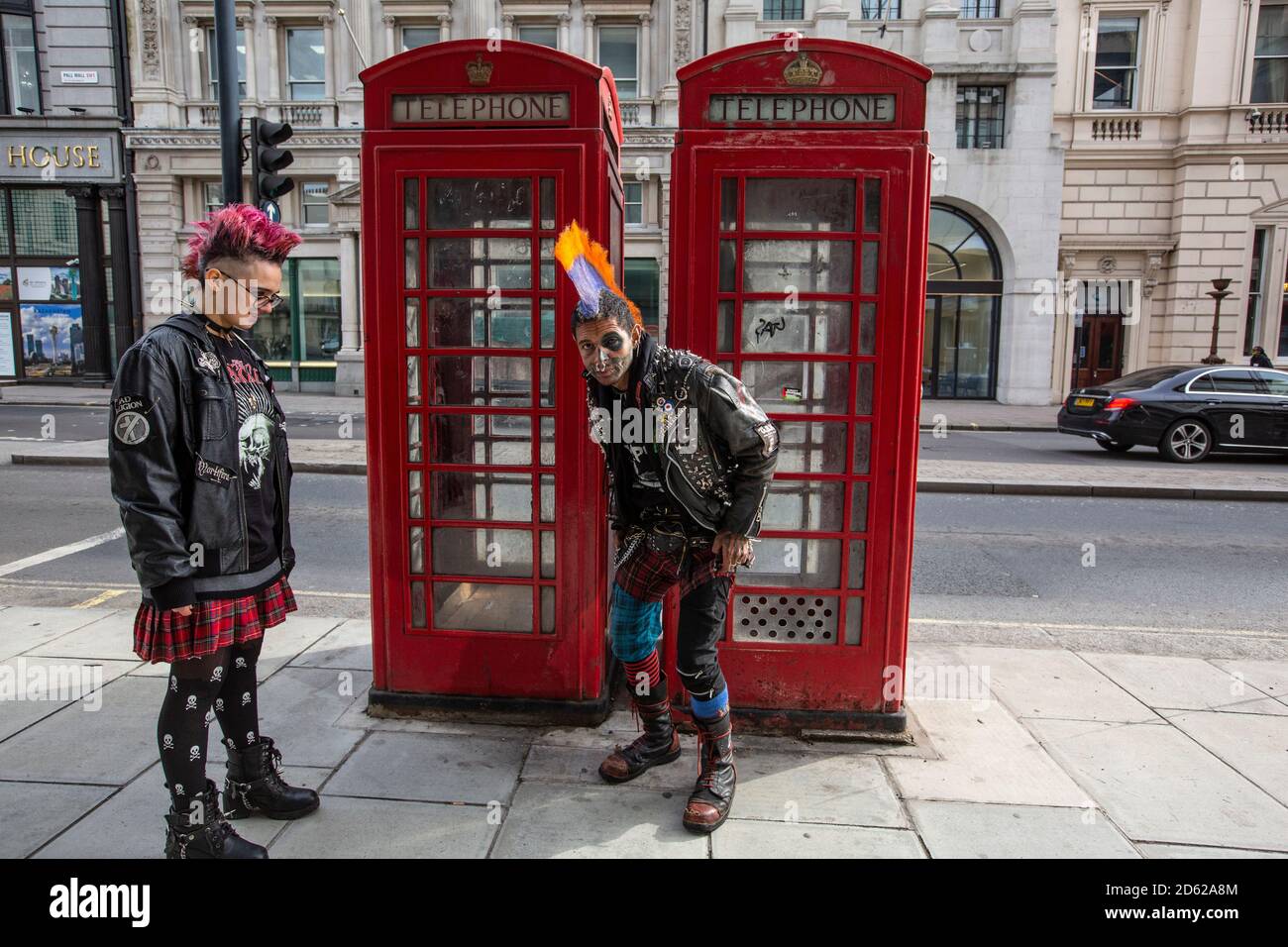 Punk rocker con capelli mohican si siede rilassante sulla parte superiore delle scatole rosse del telefono nel centro di Londra, Inghilterra, Regno Unito Foto Stock