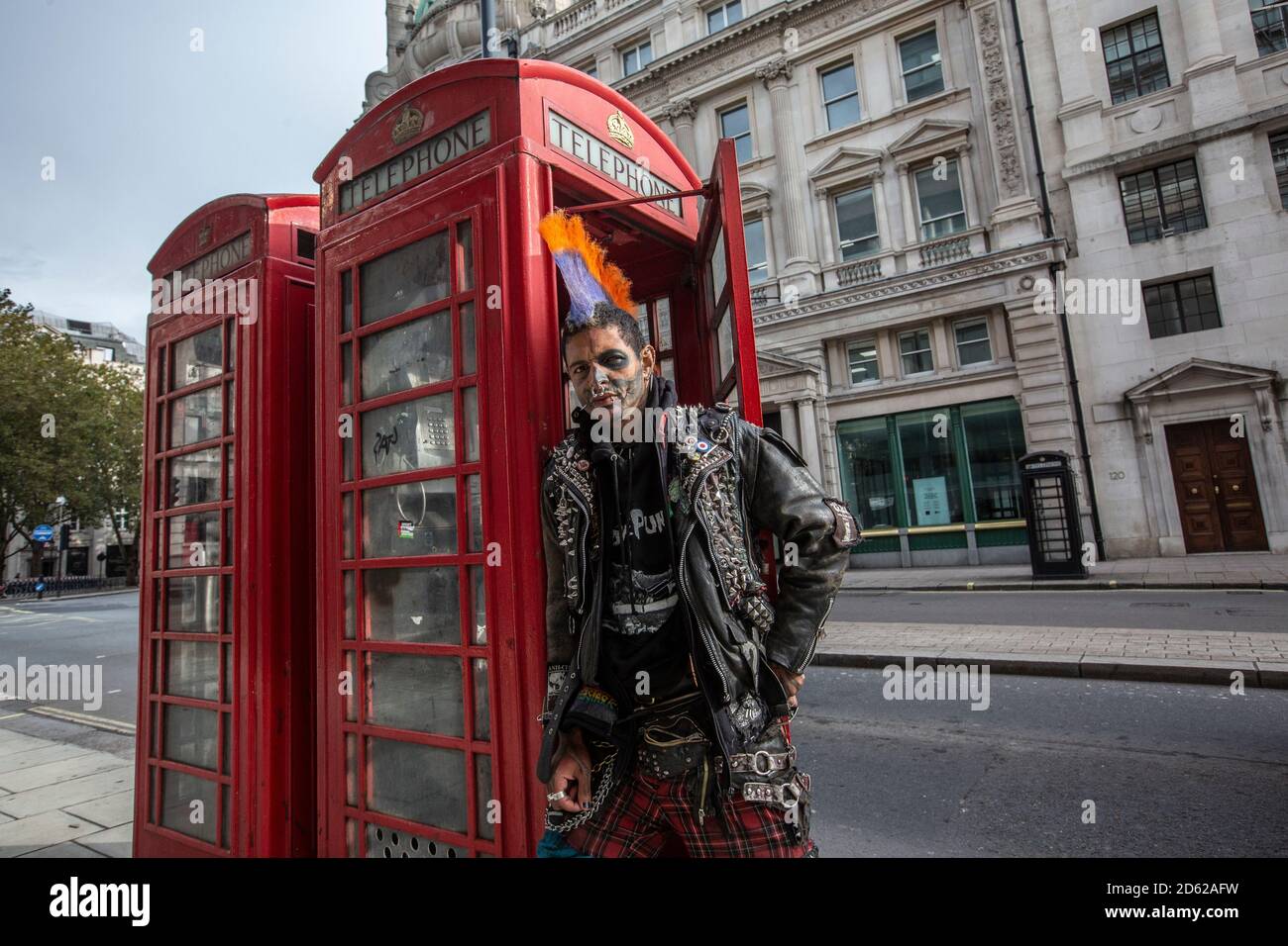 Punk rocker con capelli mohican si siede rilassante sulla parte superiore delle scatole rosse del telefono nel centro di Londra, Inghilterra, Regno Unito Foto Stock