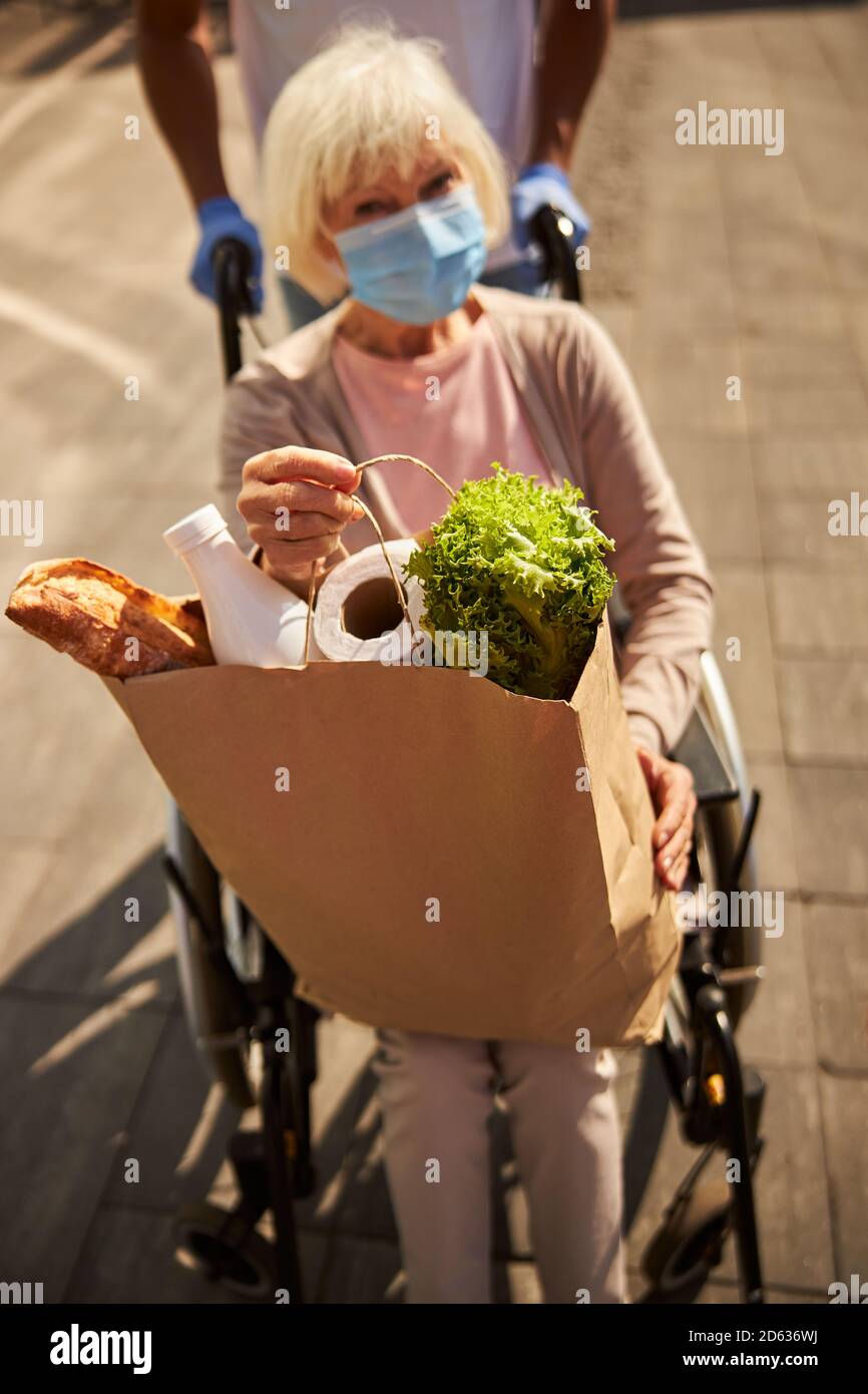 Donna anziana disabile con un sacchetto di cibo Foto Stock