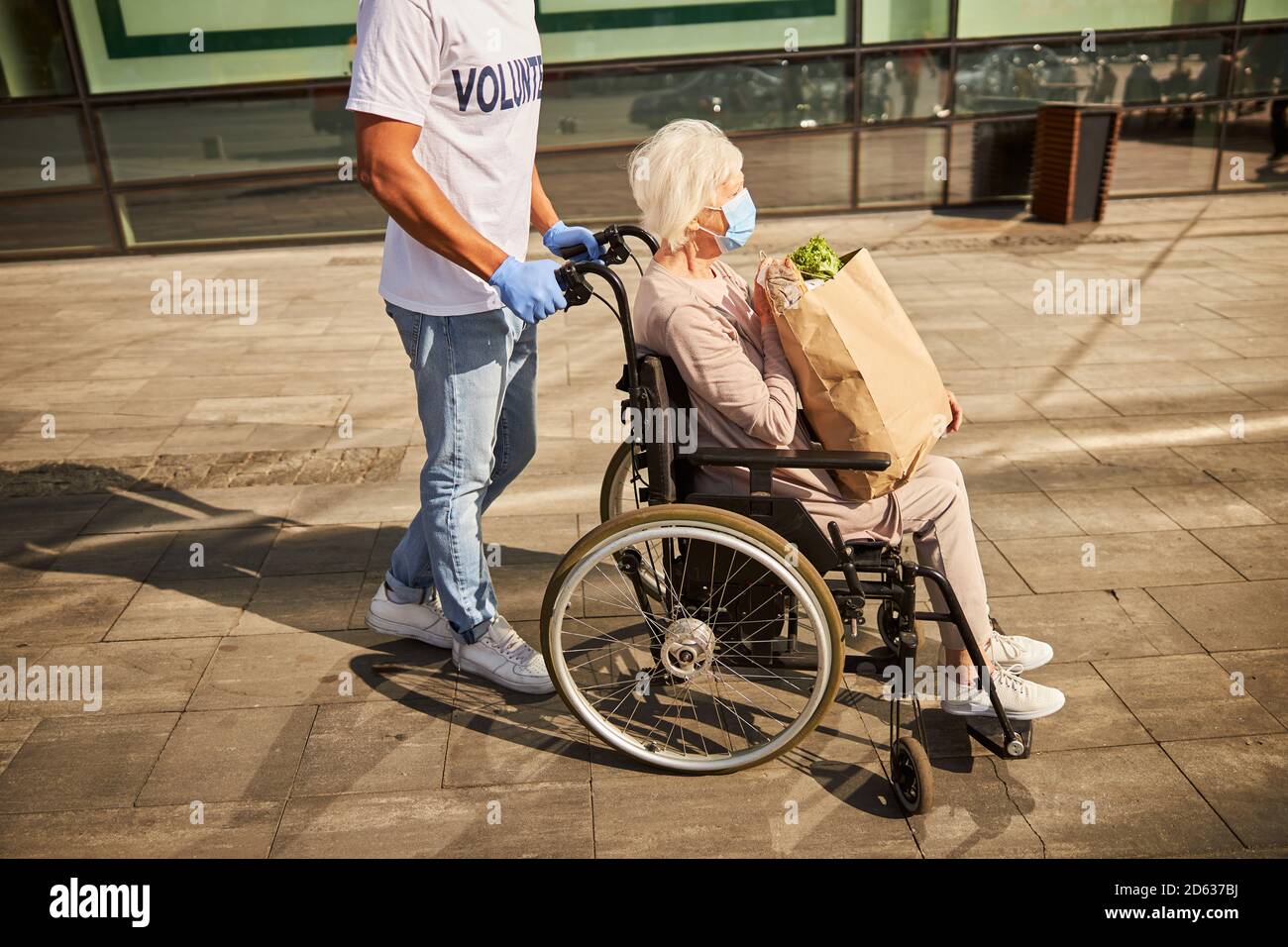 Caregiver che guida una sedia a rotelle con una signora anziana Foto Stock