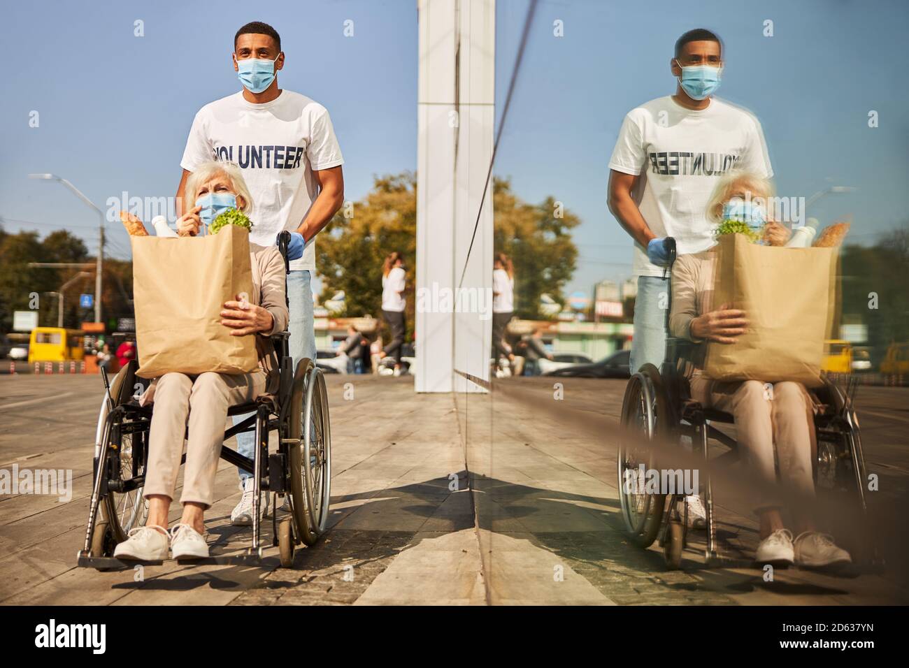 Volontario e il suo paziente anziano che riflette nella finestra del centro commerciale Foto Stock