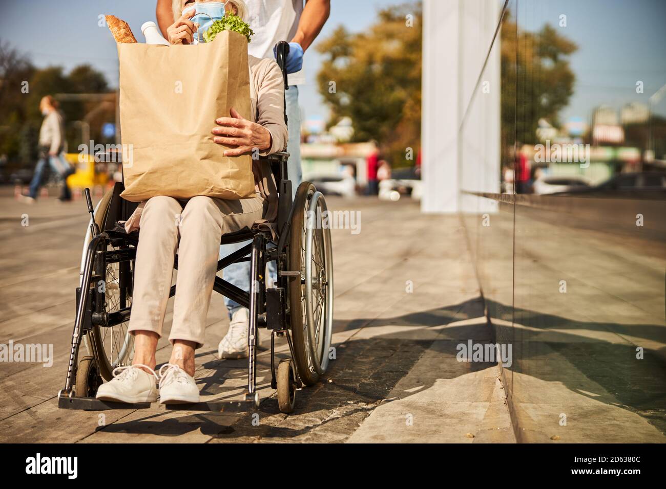 Donna anziano in sedia a rotelle che porta una busta per il cibo Foto Stock