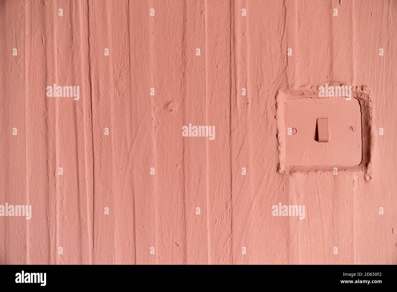 Una cornice completa di una vecchia parete in terracotta dipinta con carta da parati e linee verticali strutturate e un interruttore di leccatura Foto Stock