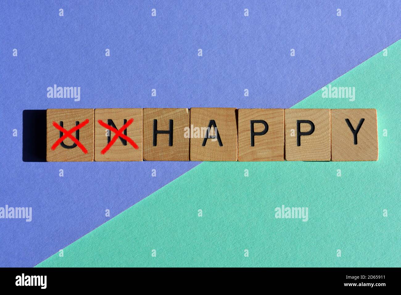 Infelice in lettere di legno con il prefisso un barrato, lasciando la parola opposta felice isolato su uno sfondo colorato Foto Stock