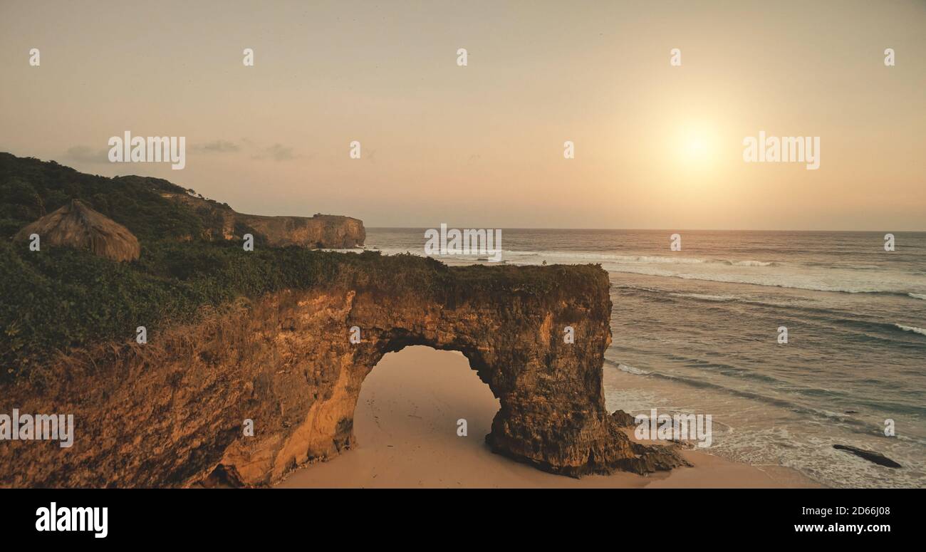 Luce del sole sulla scogliera verde sulla spiaggia di sabbia bagnata dalle onde della baia dell'oceano. Nessuno natura stagcape al mare costa. Spiaggia di roccia con solo Lodge, casa a prato verde a Sumba Island, Indonesia Foto Stock