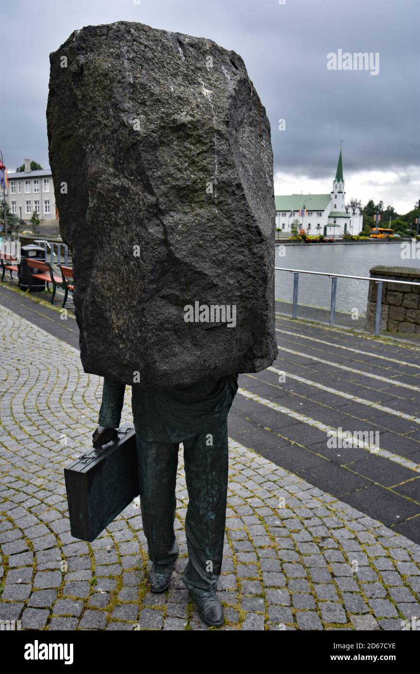Monumento al burocrate sconosciuto sul bordo del lago Tjornin, nel centro di Reykjavik, Islanda. Una grande pietra con una metà inferiore mans che tiene una valigetta Foto Stock