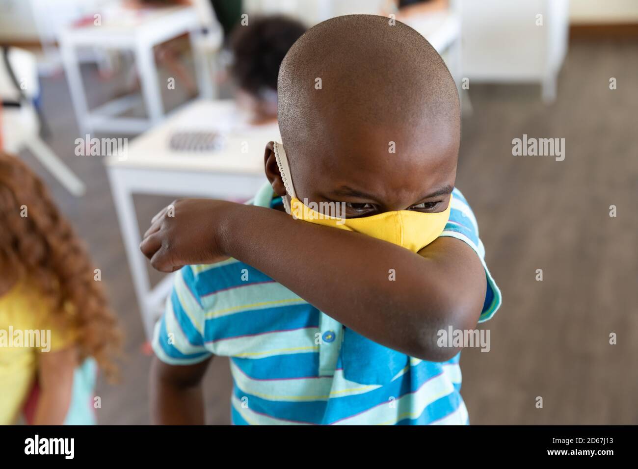 Ragazzo indossando maschera viso starnutire mentre copre la bocca a. scuola Foto Stock