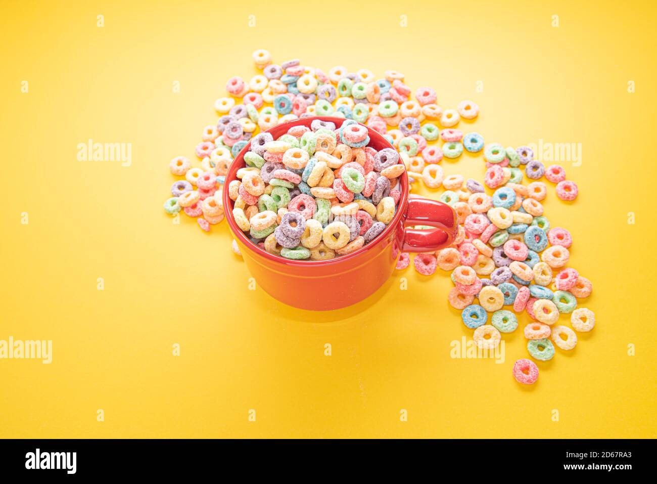 Ciotola di cereali, cereali colorati in una ciotola rossa luminosa su legno, anse di cereali su sfondo giallo. Colazione veloce o spuntino, piatto. Foto Stock