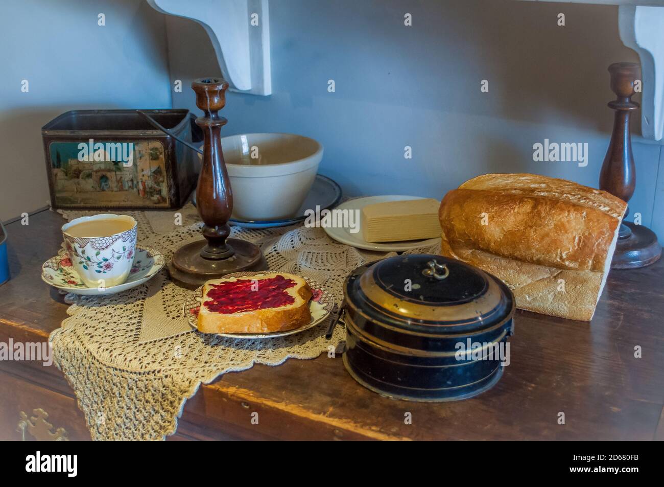 mostra museo degli anni '20 di una colazione a buffet di tè in una tazza di cina, pane, burro e marmellata, biscotto in lattina e candelabri Foto Stock