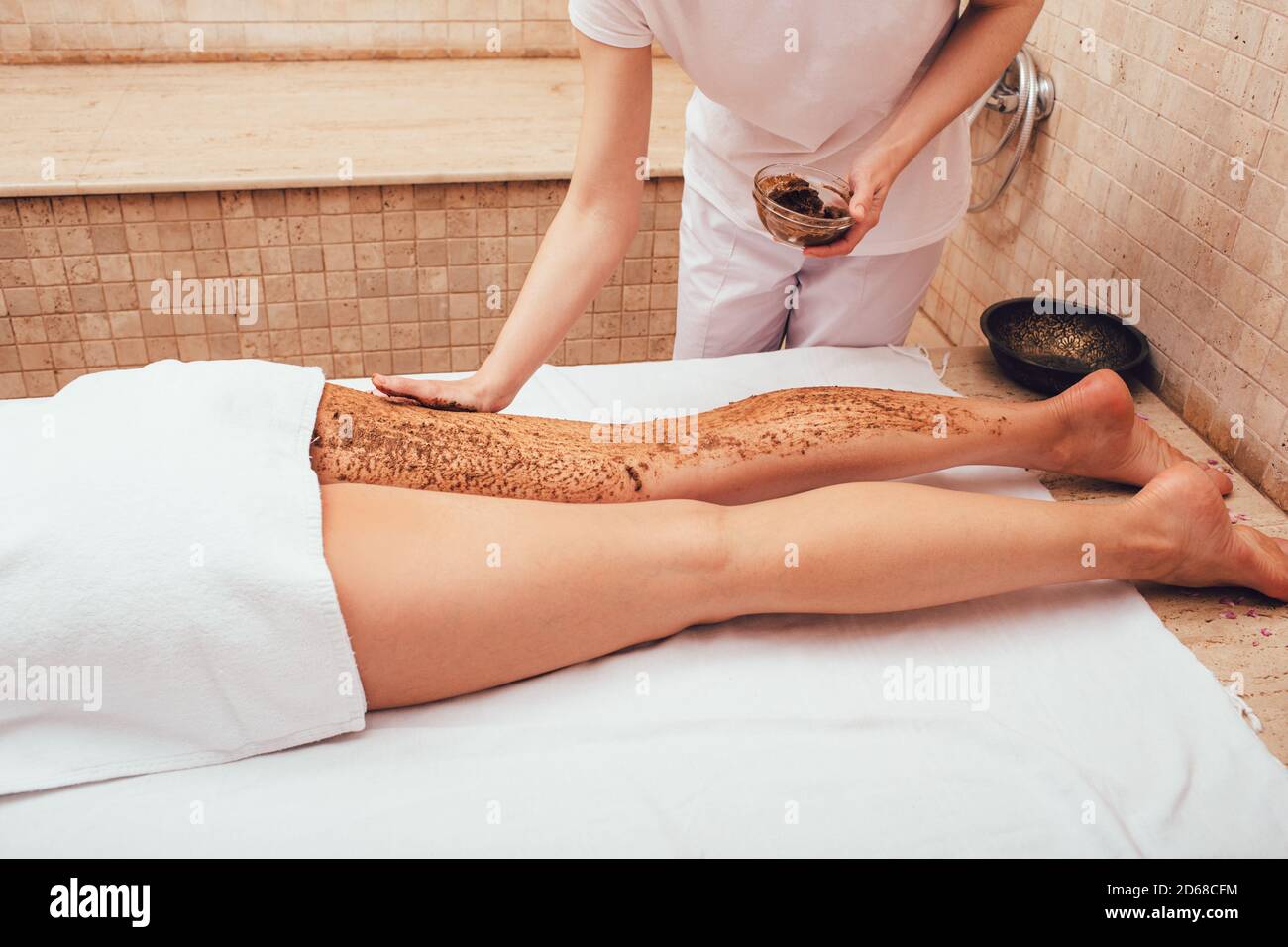 Il massaggiatore applica uno scrub di fango alle gambe di una donna. La procedura di peeling per una donna renderà le gambe lisce. Foto Stock