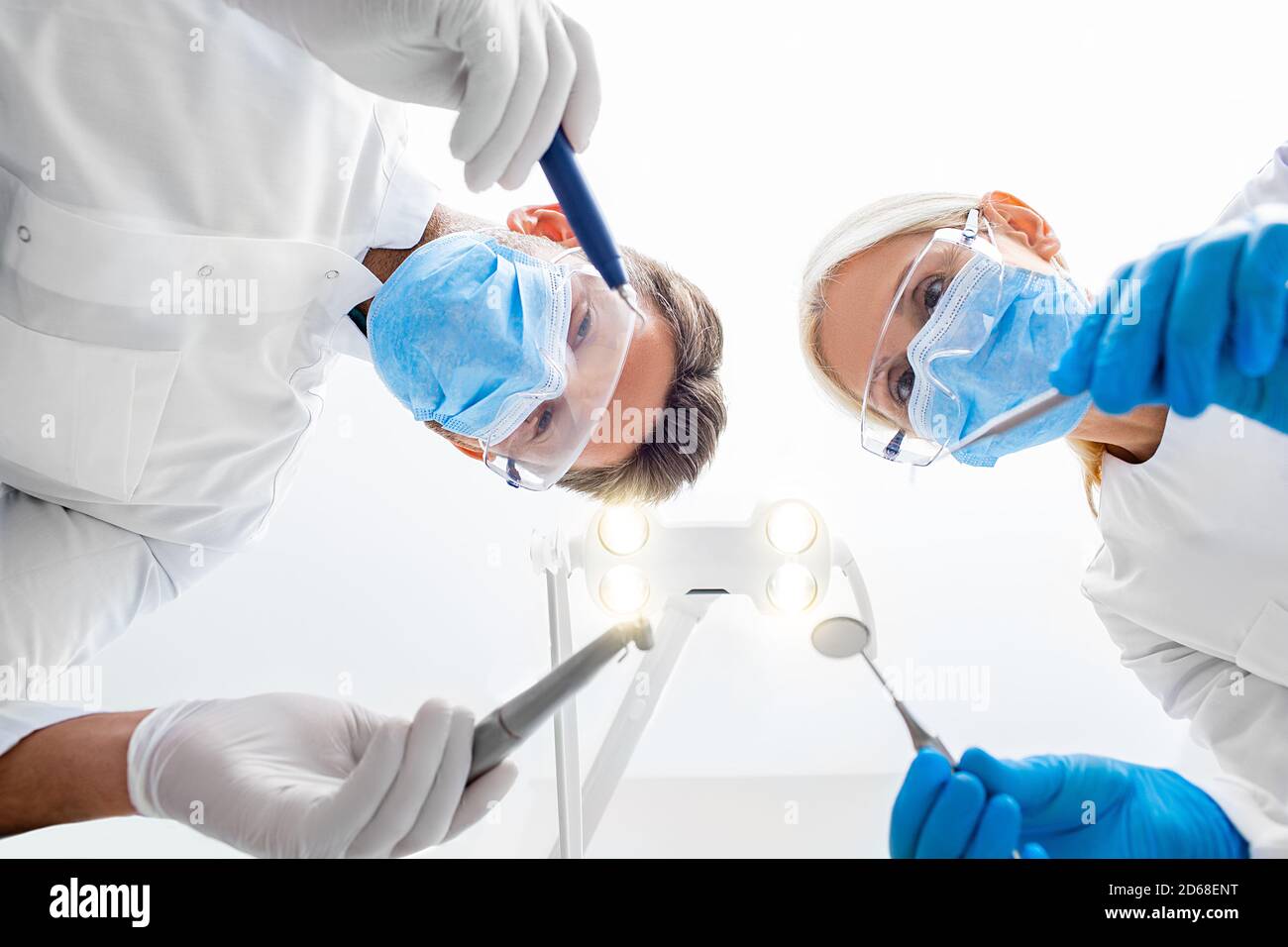 Dentista e assistente che indossa occhiali di protezione e maschera medica che regge l'attrezzatura dentale. Trattamento denti, vista dal basso. Lavoro di squadra di odontoiatria Foto Stock
