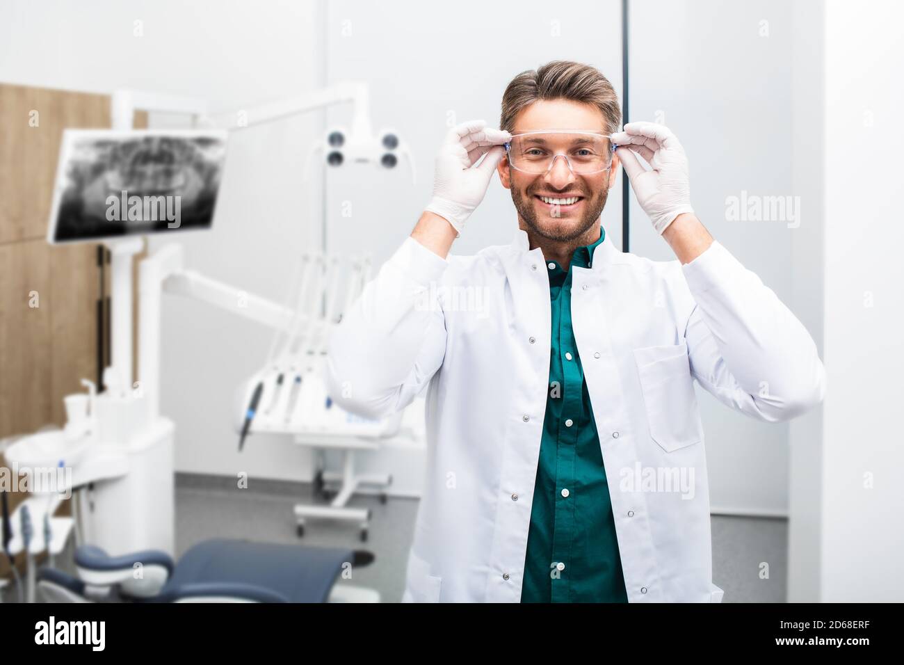 Ritratto di un bel dentista maschile sorridente che indossa occhiali protettivi in una moderna clinica dentale. Odontoiatria moderna Foto Stock