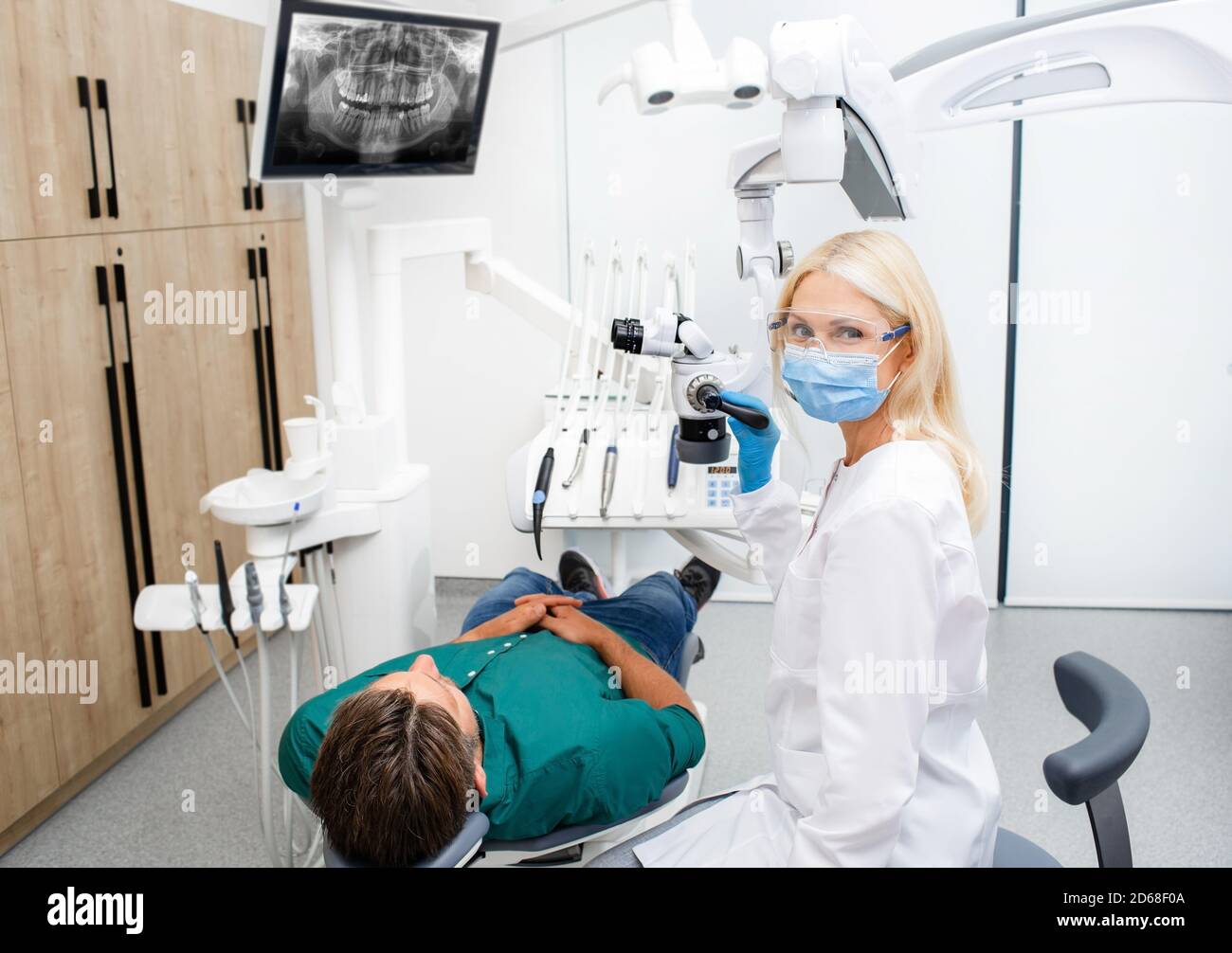 Ritratto di una bella dentista femminile in occhiali protettivi e. una maschera durante il trattamento di un paziente in uno studio dentistico Foto Stock