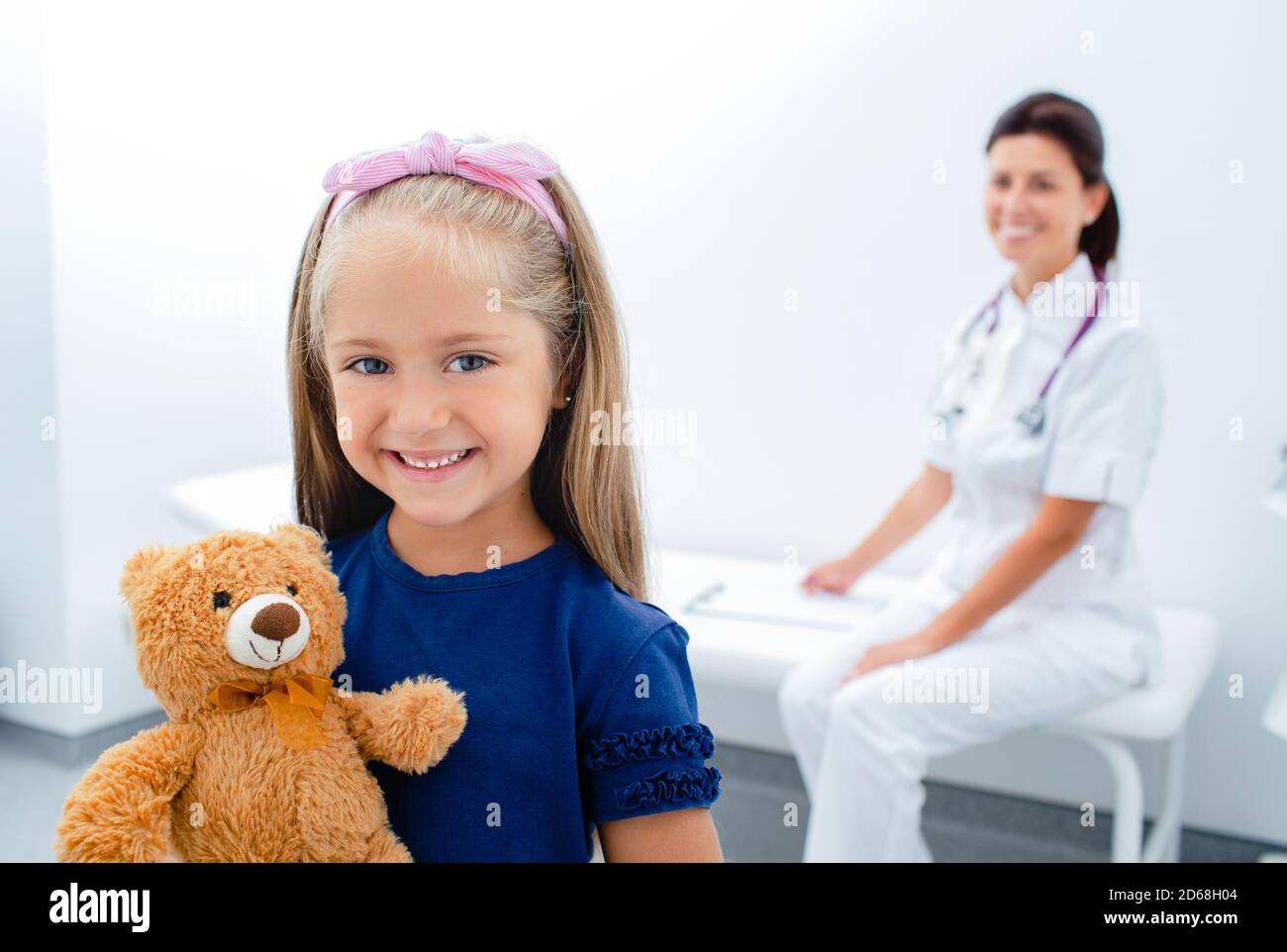 Sorridente bambina con giocattolo in piedi al reparto dell'ospedale. il dottore è seduto su un sfondo Foto Stock
