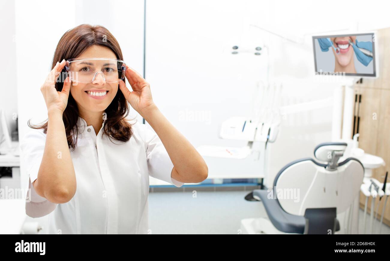 Ritratto positivo bella dentista femminile indossando occhiali protettivi presso la moderna clinica dentale. Foto Stock