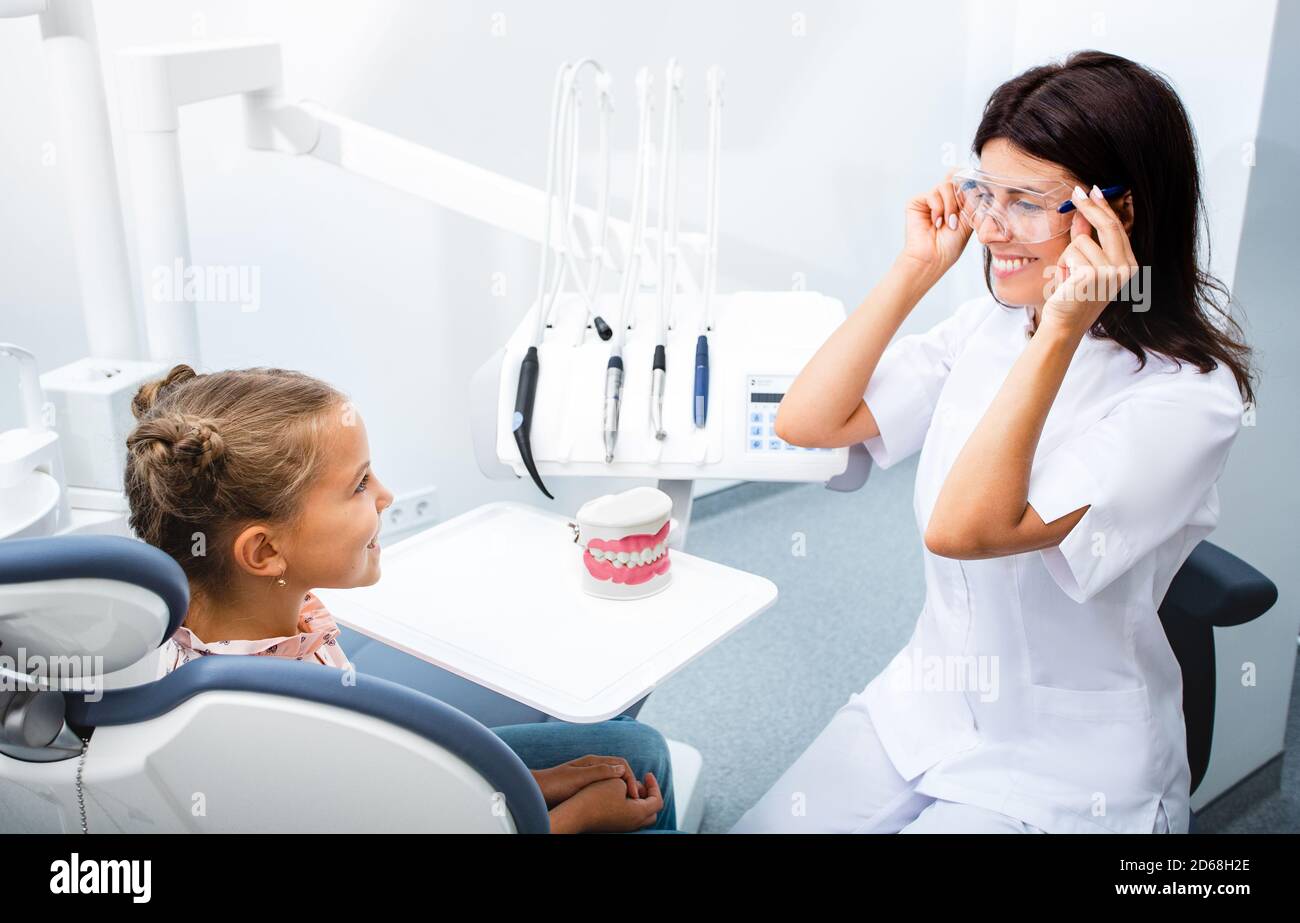 Bambina e dentista comunicano in clinica moderna. Dentista che inizia il trattamento dei denti dei bambini. Foto Stock