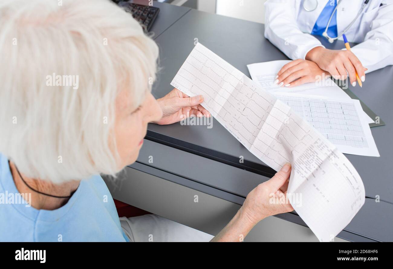 Paziente anziano che guarda i risultati di un cardiogramma del suo cuore nell'ufficio di un cardiologo. Diagnosi e trattamento di aritmie, erea coronarica Foto Stock