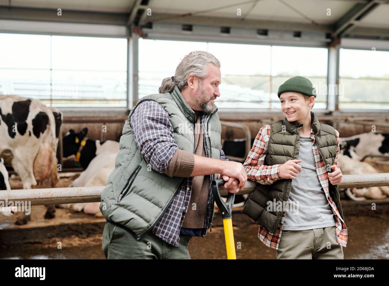 Positivo padre maturo e suo figlio poggiato sulla ringhiera di stalli e discute bestiame mentre avendo rottura alla fattoria Foto Stock