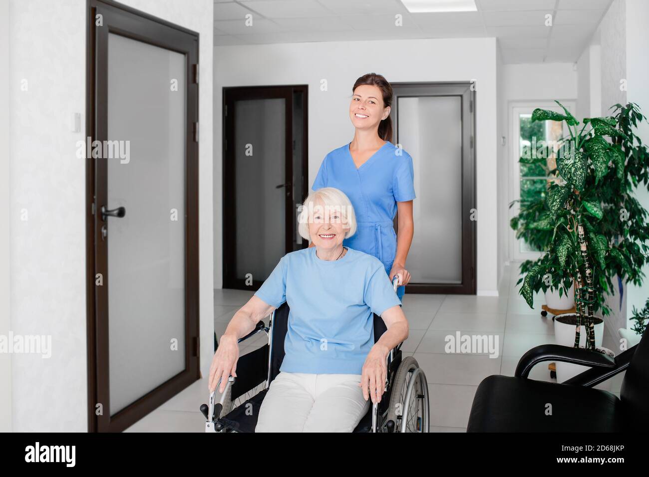 Infermiere amichevole che si prende cura del paziente anziano in un sedia a rotelle nel corridoio dell'ospedale Foto Stock