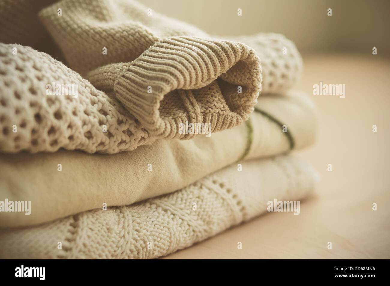 Su uno sfondo beige si trovano diversi pullover di luce calda e morbida con diversi modelli, piegati in un palo pulito, e in cima è la manica di un altro maglione Foto Stock