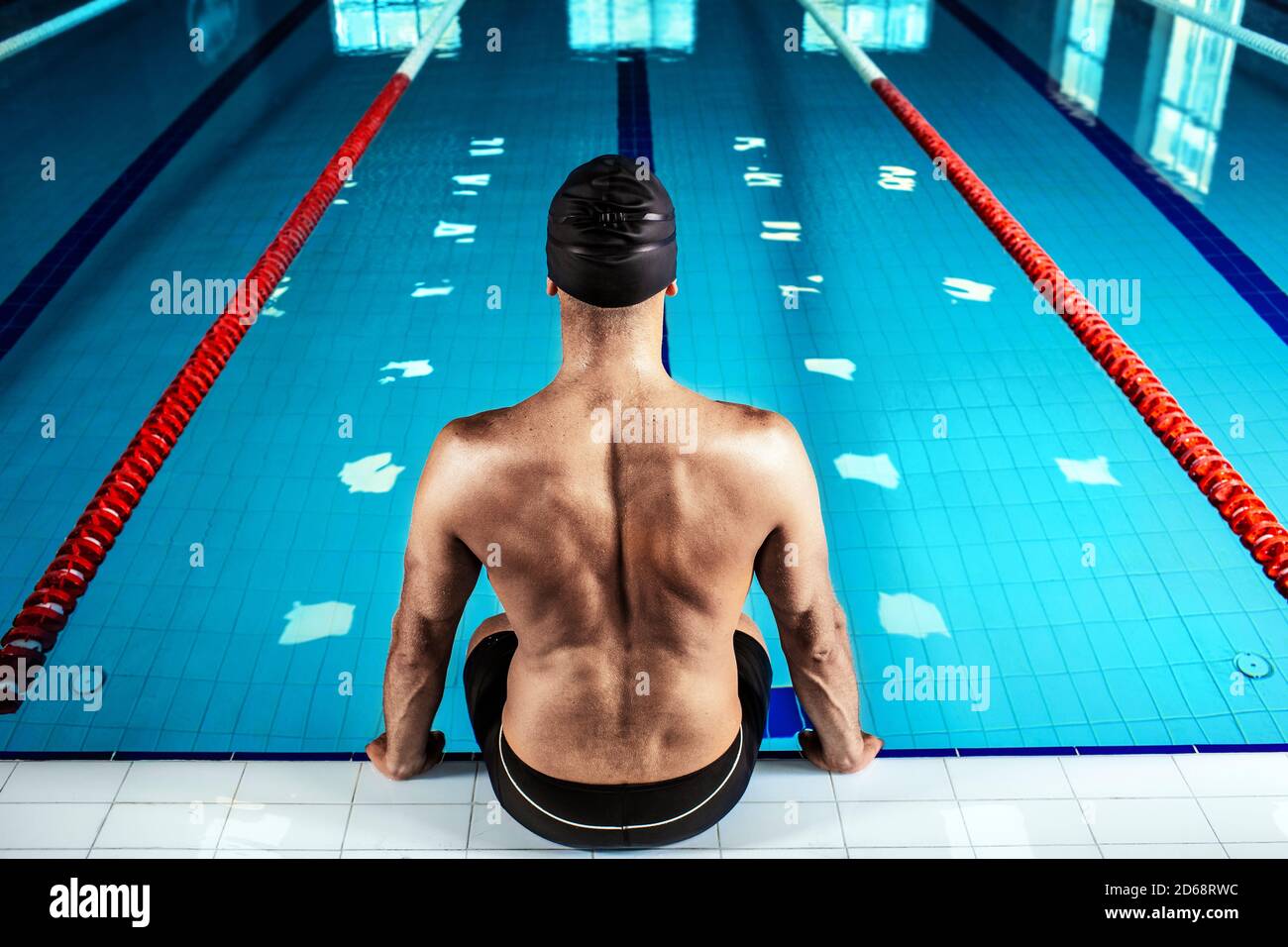 Nuotatore seduto a bordo piscina, vista sul retro. Nuotatore professionista vicino alla piscina, forte contrasto Foto Stock
