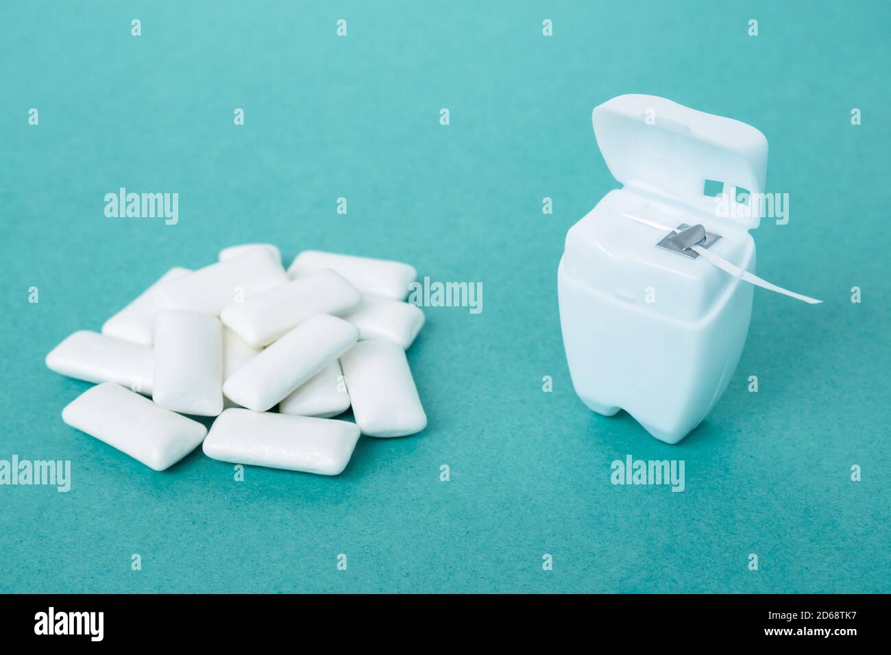 filo interdentale in contenitore bianco e mucchio di gomme da masticare su sfondo blu Foto Stock