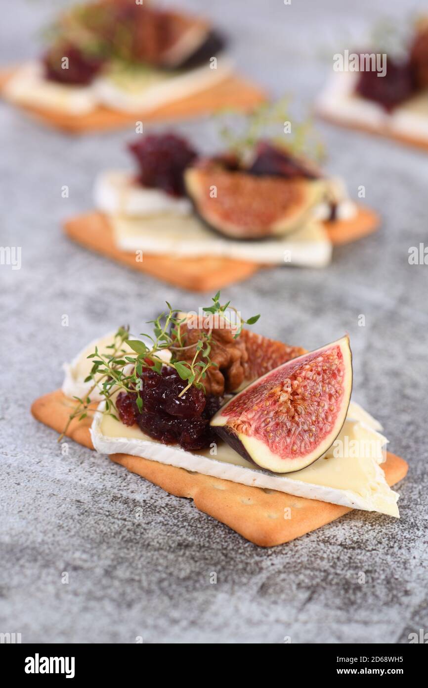 Cracker con una fetta di camembert, marmellata, fichi e noci. Un'ottima idea di spuntino per una vacanza, un picnic o una festa. Foto Stock