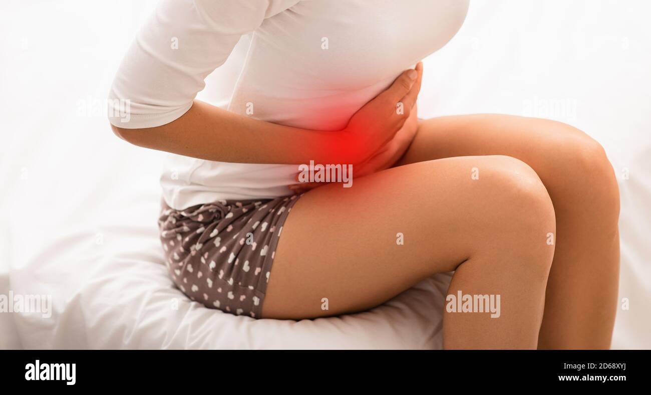 Donna che soffre di dolore mestruale, mentre si siede a letto. Dolore allo stomaco Foto Stock