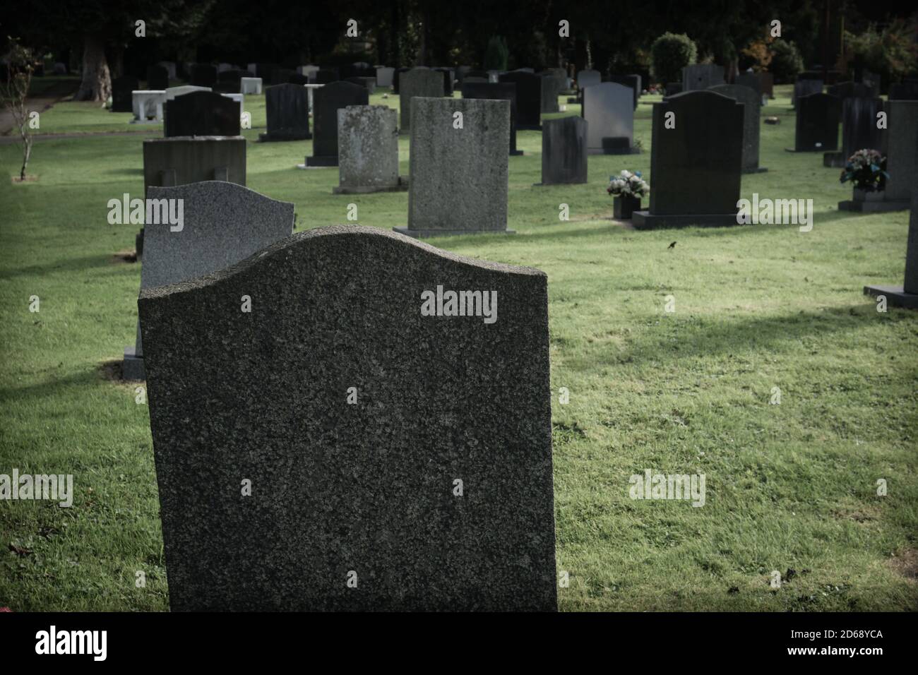 Pietre di tomba vuote o marcatori in un cimitero con un filtro scuro e cupo applicato all'immagine Foto Stock