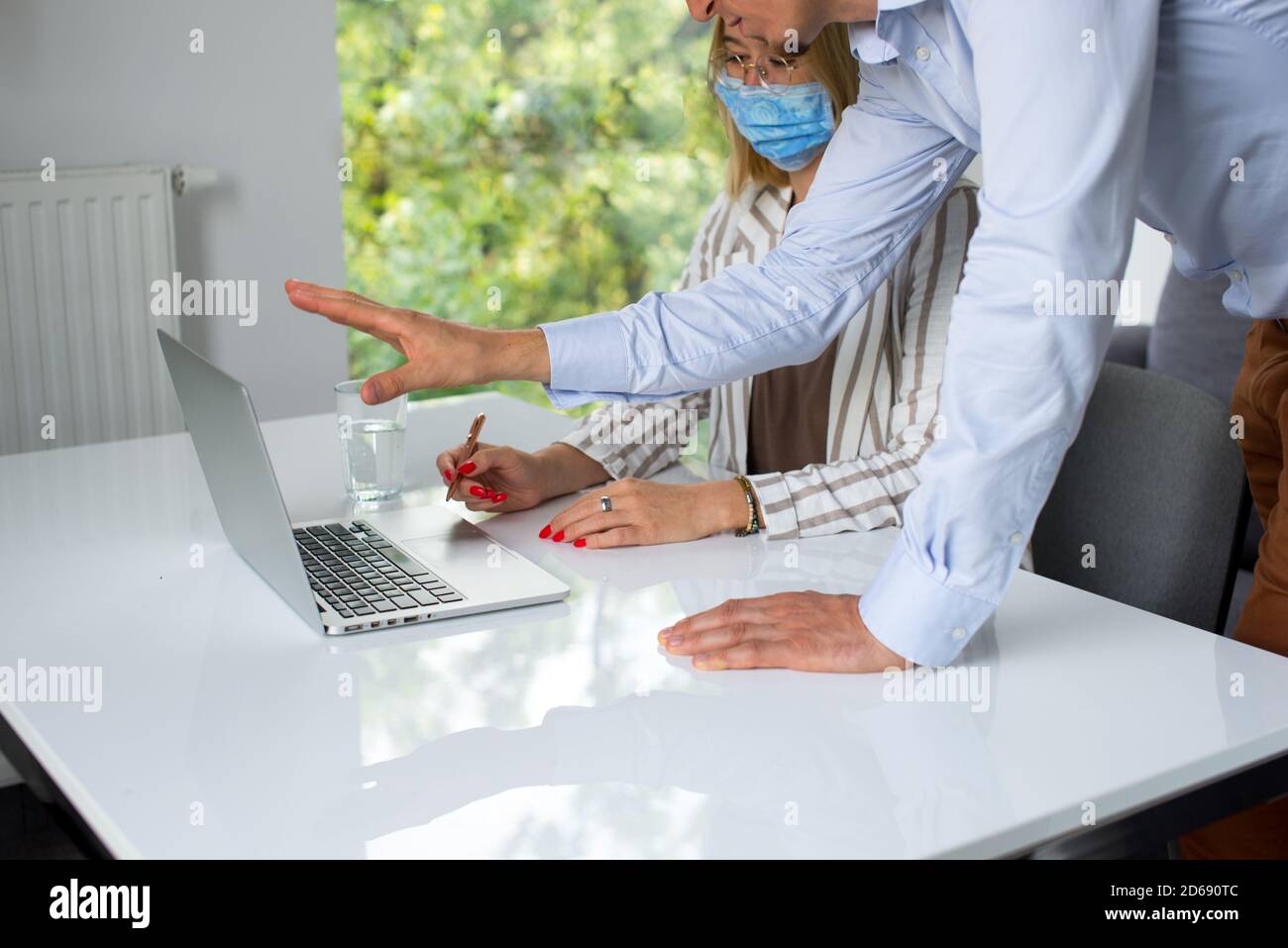 Uomini d'affari, donne e uomini con maschera aganista covid che parla di fronte al computer portatile in sala di lavoro. Coronavirus nel lavoro. Covid-19 in ufficio. Buissnes Foto Stock