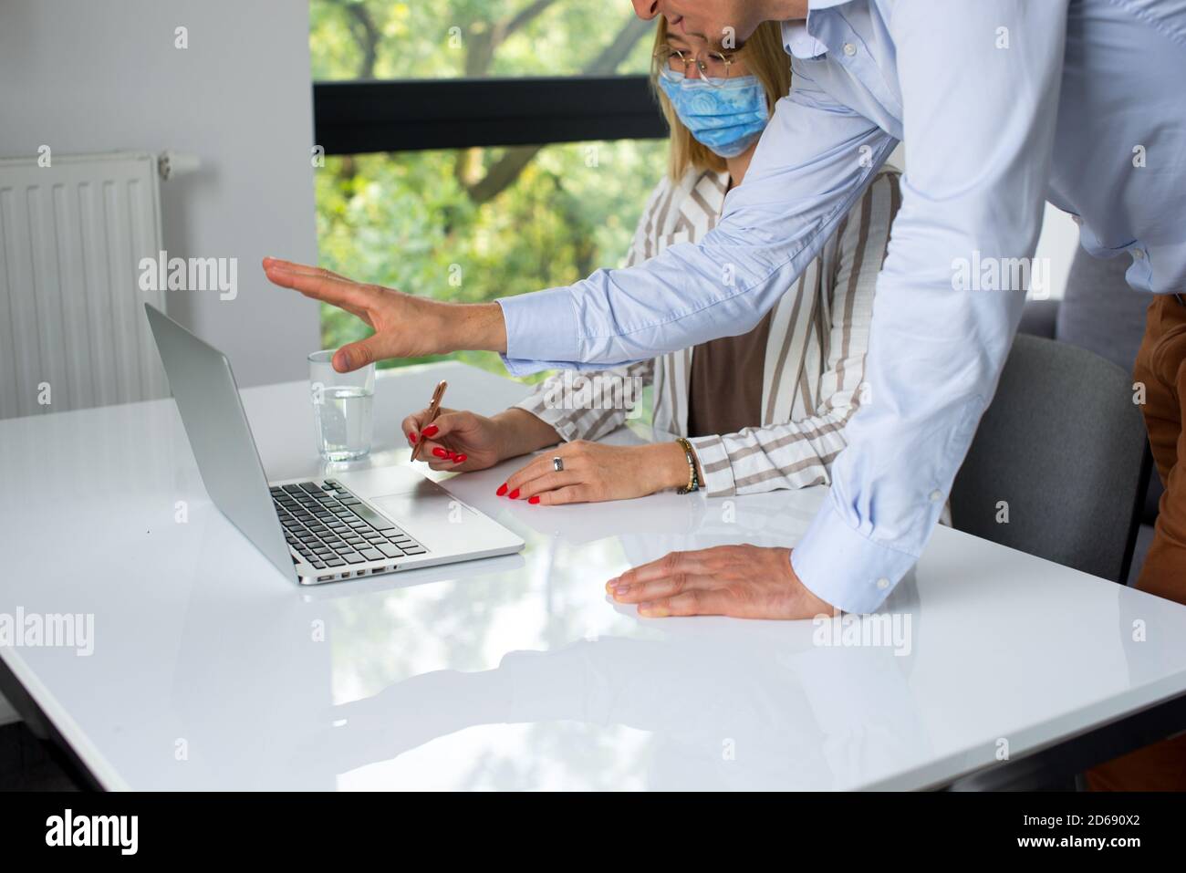 Uomini d'affari, donne e uomini con maschera aganista covid che parla di fronte al computer portatile in sala di lavoro. Coronavirus nel lavoro. Covid-19 in ufficio. Buissnes Foto Stock