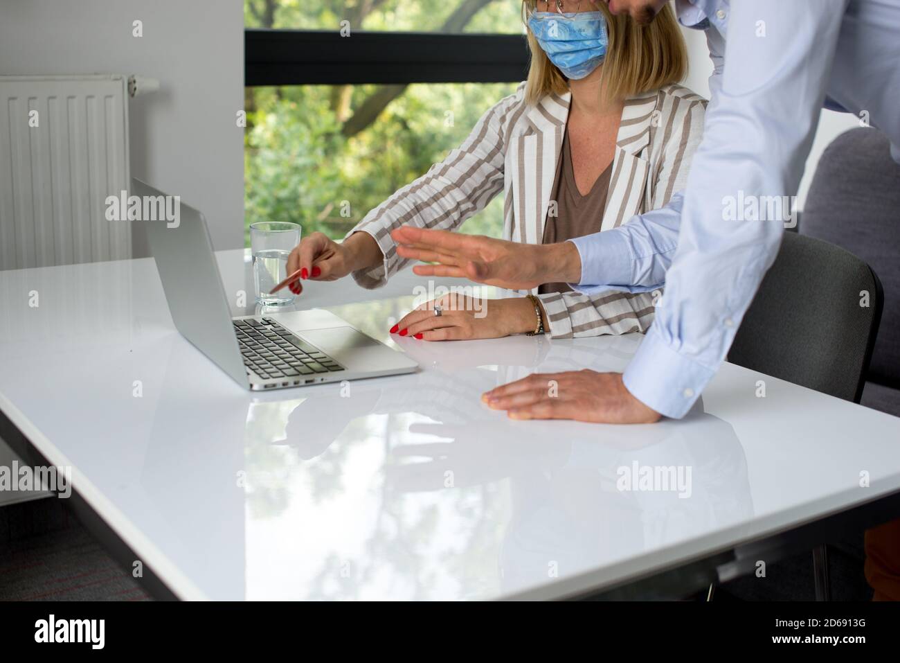 Uomini d'affari, donne e uomini con maschera aganista covid che parla di fronte al computer portatile in sala di lavoro. Coronavirus nel lavoro. Covid-19 in ufficio. Buissnes Foto Stock