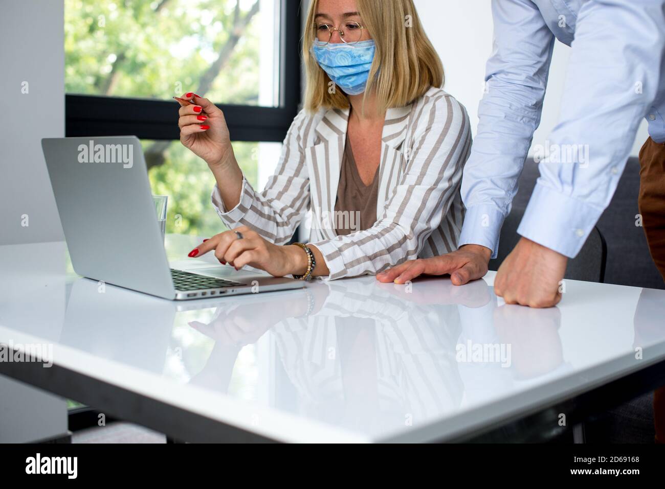 Uomini d'affari, donne e uomini con maschera aganista covid che parla di fronte al computer portatile in sala di lavoro. Coronavirus nel lavoro. Covid-19 in ufficio. Buissnes Foto Stock