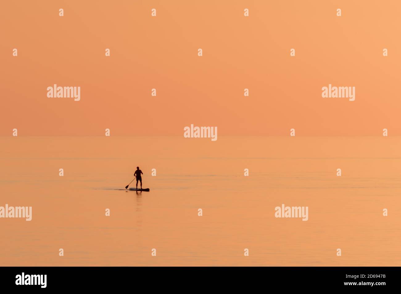 Silhouette di sola persona che pratica il paddle surf su una spiaggia solitaria al tramonto. Foto Stock
