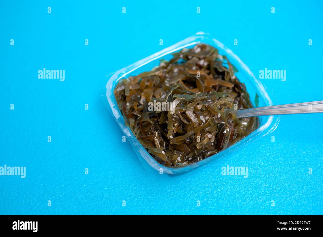 Una deliziosa insalata di alghe fresche. Insalata di alghe commestibili e forchetta su sfondo blu. Foto Stock