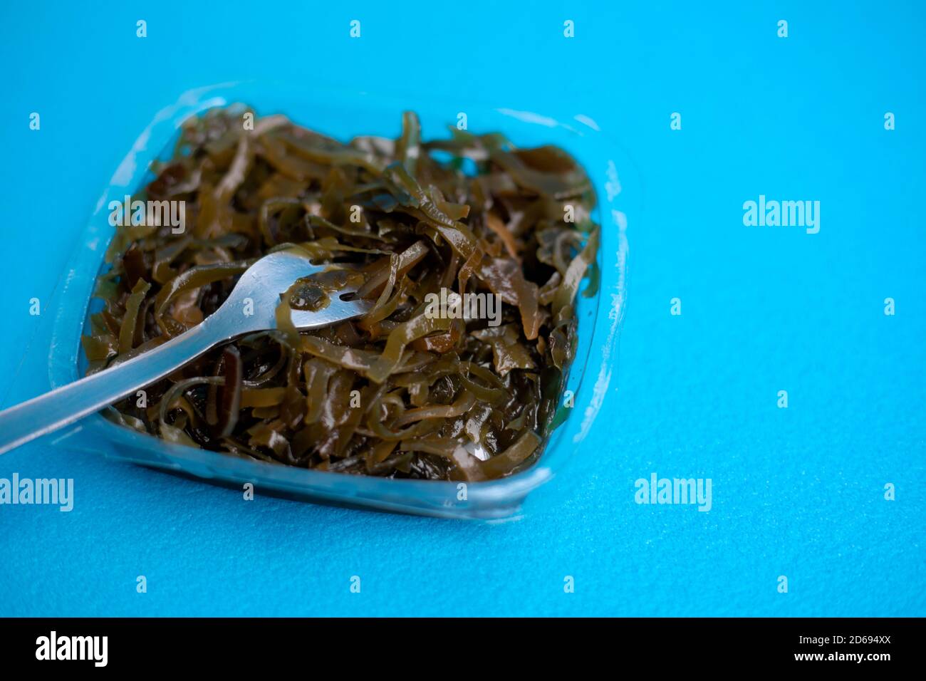Una deliziosa insalata di alghe fresche. Insalata di alghe commestibili e forchetta su sfondo blu. Foto Stock