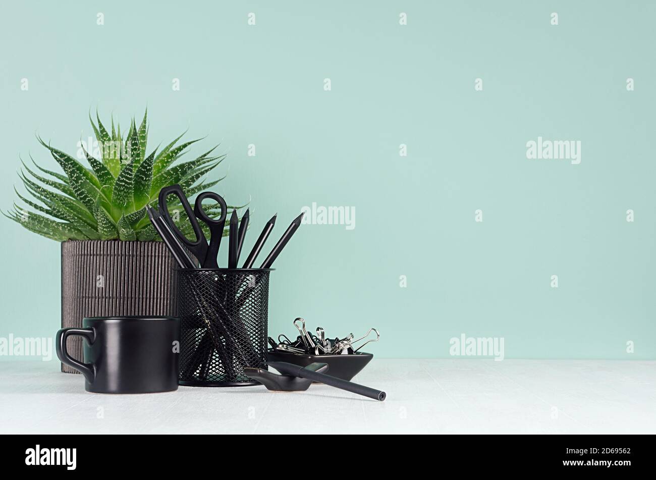 Casa ufficio di primavera per affari e studio con cancelleria nera, caffè tazza, aloe pianta, matite in verde chiaro menthe interno su legno bianco des Foto Stock