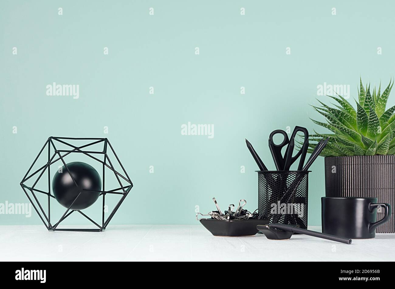 Interni domestici - posto di lavoro con cancelleria nera, pianta della casa verde, tazza del caffè, pianta dell'aloe, modello astratto dell'atomo in colore della menta verde su WO bianco Foto Stock