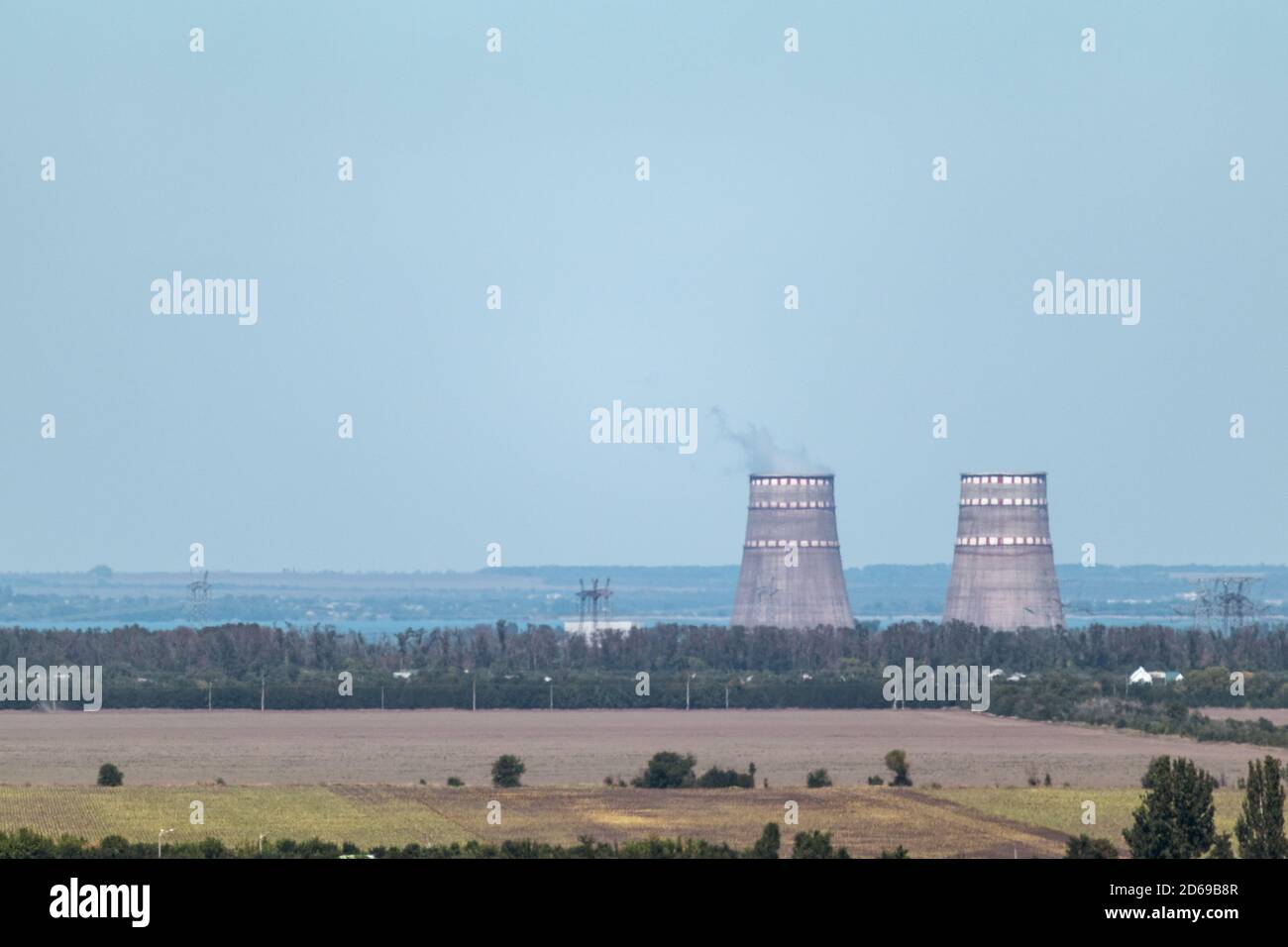 Paesaggio rurale blu con due grandi tubi di fabbrica a distanza. Fumo industriale che inquina l'aria. Foto Stock